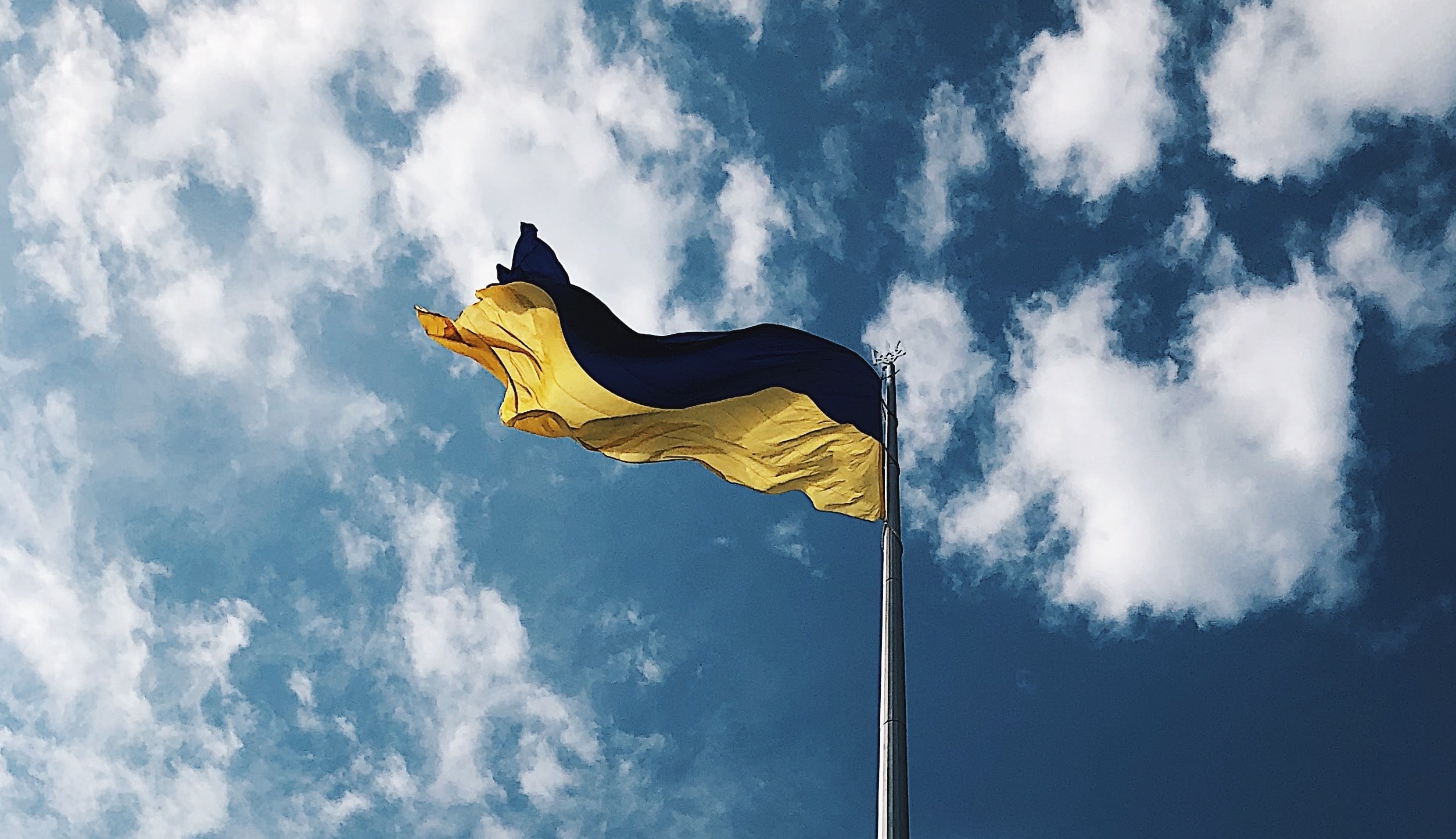 Blue and yellow Ukrainian flag flying against blue sky with clouds